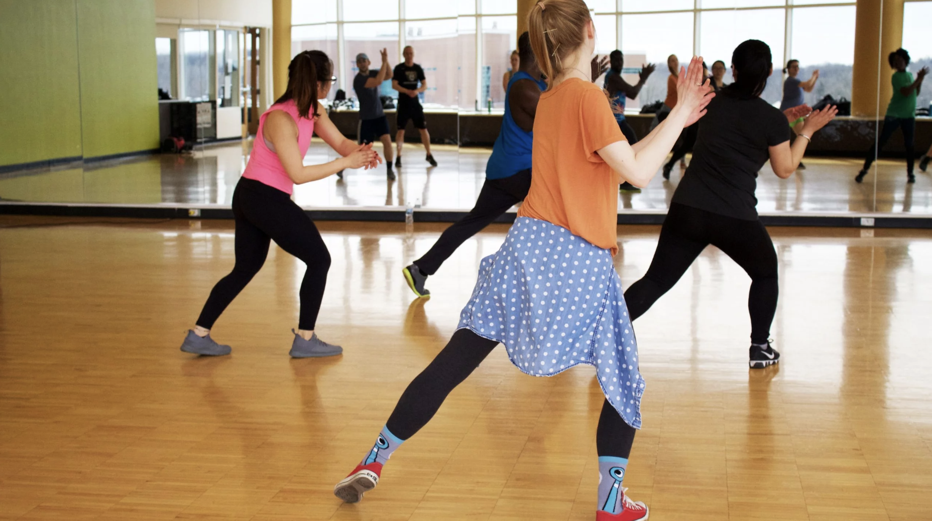 Group of people dance in a dance studio and face a mirror.